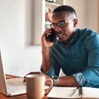 A man talking on the phone and looking at a laptop