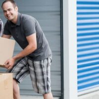 Two smiling people putting boxes in a self storage unit